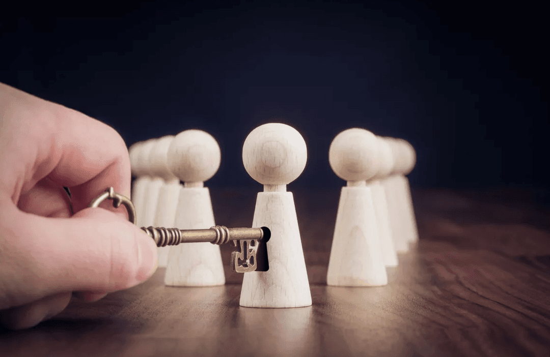 A hand using a small key to unlock one of several wooden figures